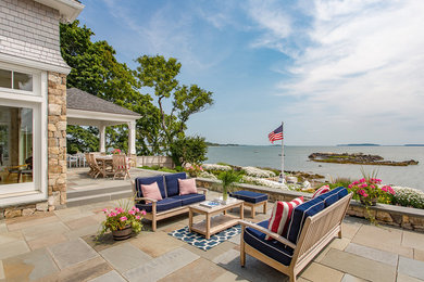 This is an example of an expansive beach style backyard patio in Boston with natural stone pavers and a roof extension.