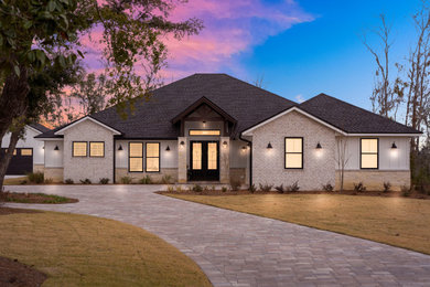 Large cottage white one-story brick house exterior photo in Other with a hip roof, a shingle roof and a black roof