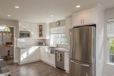 Open concept kitchen - mid-sized transitional galley light wood floor and beige floor open concept kitchen idea in San Francisco with a farmhouse sink, shaker cabinets, white cabinets, quartzite countertops, white backsplash, porcelain backsplash, stainless steel appliances, a peninsula and white countertops