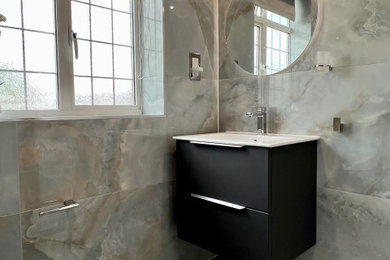 Photo of a medium sized contemporary grey and teal bathroom in London with flat-panel cabinets, black cabinets, a freestanding bath, a walk-in shower, a wall mounted toilet, grey tiles, porcelain tiles, white walls, porcelain flooring, a wall-mounted sink, grey floors, a hinged door, white worktops, a feature wall, a single sink, a floating vanity unit and a vaulted ceiling.