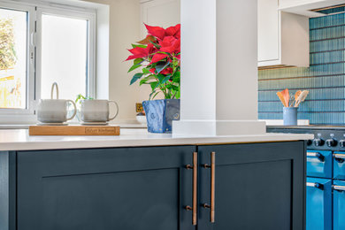 Photo of a large contemporary u-shaped kitchen/diner in Sussex with a belfast sink, shaker cabinets, blue cabinets, quartz worktops, blue splashback, coloured appliances, limestone flooring, an island, beige floors, white worktops, a vaulted ceiling and feature lighting.