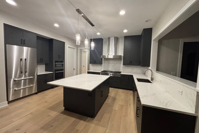 Minimalist light wood floor kitchen photo in Chicago with a single-bowl sink, flat-panel cabinets, black cabinets, quartz countertops, white backsplash, quartz backsplash, stainless steel appliances, an island and white countertops