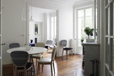 Cette photo montre une salle à manger ouverte sur le salon tendance de taille moyenne avec un mur blanc, un sol en bois brun, une cheminée standard, un manteau de cheminée en pierre et un sol marron.
