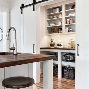 Modelo de cocina en L, campestre, grande, cerrada, con puertas de armario blancas, encimera de madera, salpicadero blanco, salpicadero de azulejos tipo metro, suelo de madera en tonos medios, suelo marrón, encimeras marrones, fregadero sobremueble, electrodomésticos de acero inoxidable, una isla y armarios estilo shaker