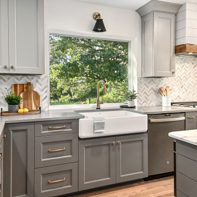 Eat-in kitchen - huge cottage l-shaped medium tone wood floor and brown floor eat-in kitchen idea in Milwaukee with a farmhouse sink, shaker cabinets, gray cabinets, quartz countertops, white backsplash, marble backsplash, stainless steel appliances, an island and gray countertops