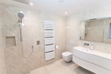 This is an example of a small modern ensuite wet room bathroom in Devon with a wall mounted toilet, multi-coloured tiles, ceramic flooring, a wall-mounted sink, an open shower and a built in vanity unit.
