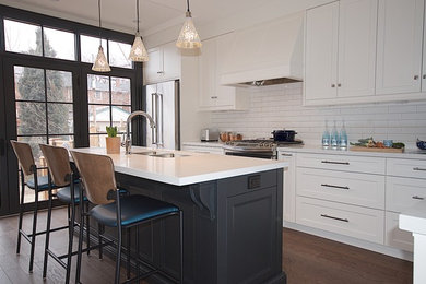 This is an example of a contemporary l-shaped eat-in kitchen in Toronto with an undermount sink, recessed-panel cabinets, white cabinets, quartz benchtops, white splashback, ceramic splashback, stainless steel appliances, dark hardwood floors, with island and brown floor.