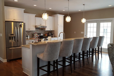 Huge transitional single-wall dark wood floor open concept kitchen photo in Other with an undermount sink, raised-panel cabinets, white cabinets, quartz countertops, beige backsplash, mosaic tile backsplash, stainless steel appliances and an island