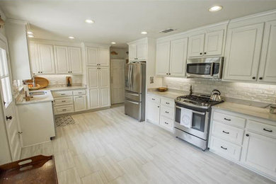 Example of a large classic l-shaped porcelain tile and gray floor eat-in kitchen design in New Orleans with a double-bowl sink, raised-panel cabinets, white cabinets, marble countertops, white backsplash, subway tile backsplash, stainless steel appliances and no island