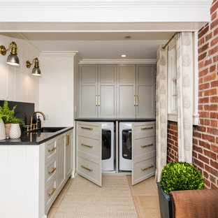 Inspiration for a small traditional l-shaped utility room in DC Metro with a submerged sink, recessed-panel cabinets, grey cabinets, granite worktops, white walls, ceramic flooring, a concealed washer and dryer and beige floors.