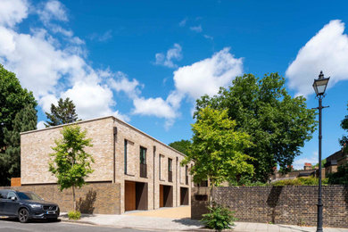 Large and beige contemporary brick terraced house in London with three floors, a flat roof and a grey roof.
