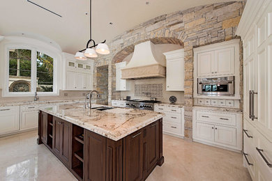 Open concept kitchen - huge mediterranean u-shaped travertine floor and beige floor open concept kitchen idea in Miami with beaded inset cabinets, granite countertops, an undermount sink, white cabinets, beige backsplash, stainless steel appliances and an island