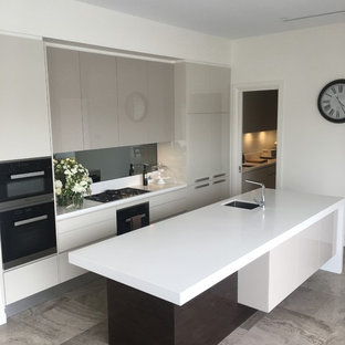 Idée de décoration pour une grande arrière-cuisine parallèle minimaliste avec un évier posé, un plan de travail en quartz, une crédence blanche, une crédence en carreau de céramique, un sol en travertin, un îlot central, un sol gris, un électroménager en acier inoxydable et un plan de travail blanc.