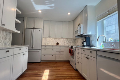 Example of a mid-sized u-shaped medium tone wood floor eat-in kitchen design in Denver with an undermount sink, shaker cabinets, white cabinets, quartz countertops, gray backsplash, glass tile backsplash, white appliances, no island and white countertops