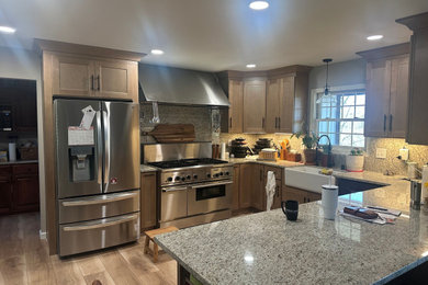 Eat-in kitchen - mid-sized u-shaped vinyl floor eat-in kitchen idea in Other with a farmhouse sink, shaker cabinets, medium tone wood cabinets, granite countertops, granite backsplash, stainless steel appliances and a peninsula