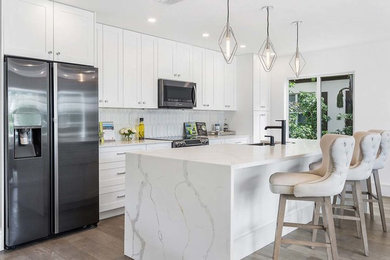 Inspiration for a mid-sized modern single-wall medium tone wood floor and brown floor eat-in kitchen remodel with an undermount sink, shaker cabinets, white cabinets, quartz countertops, white backsplash, subway tile backsplash, stainless steel appliances, an island and white countertops
