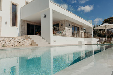 Modelo de piscina infinita mediterránea grande rectangular en patio lateral con paisajismo de piscina y suelo de baldosas