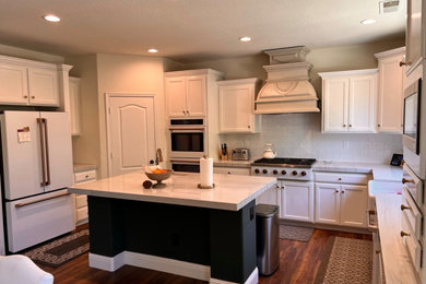 Inspiration for a timeless u-shaped laminate floor and brown floor eat-in kitchen remodel in Other with a farmhouse sink, recessed-panel cabinets, white cabinets, quartzite countertops, white backsplash, ceramic backsplash, white appliances, an island and white countertops