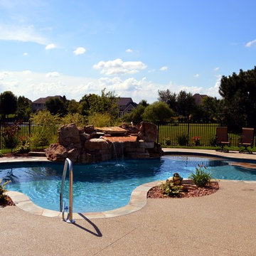 Free form pool with stone table, sun shelf, water feature, and outdoor kitchen,