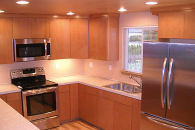 Small trendy u-shaped medium tone wood floor enclosed kitchen photo in Seattle with a drop-in sink, flat-panel cabinets, medium tone wood cabinets, solid surface countertops, beige backsplash, stainless steel appliances and a peninsula