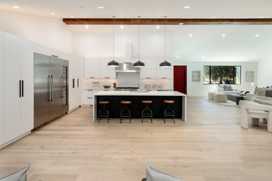Open concept kitchen - cottage l-shaped light wood floor open concept kitchen idea in San Francisco with an undermount sink, flat-panel cabinets, white cabinets, quartzite countertops, white backsplash, stainless steel appliances, an island and white countertops