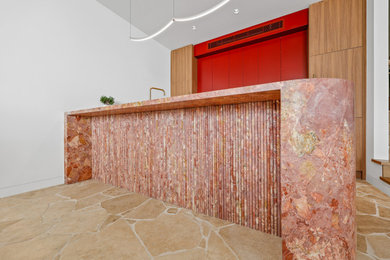 Large contemporary galley open plan kitchen in Sydney with an undermount sink, red cabinets, marble benchtops, black splashback, glass sheet splashback, black appliances, travertine floors, with island, yellow floor and pink benchtop.