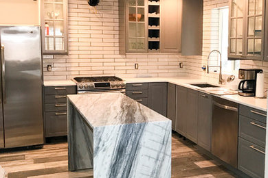 Large transitional l-shaped dark wood floor and brown floor enclosed kitchen photo in Other with an undermount sink, raised-panel cabinets, gray cabinets, solid surface countertops, white backsplash, subway tile backsplash, stainless steel appliances and an island