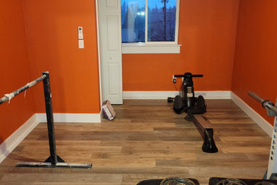 Example of a mid-sized medium tone wood floor and brown floor home weight room design in Portland with orange walls