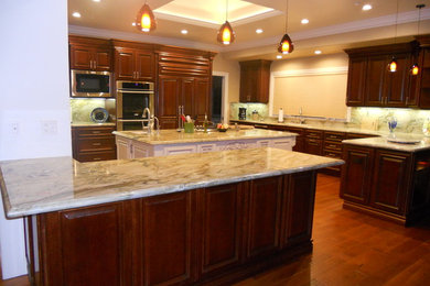 Huge elegant u-shaped dark wood floor and brown floor enclosed kitchen photo in San Francisco with an undermount sink, raised-panel cabinets, dark wood cabinets, quartzite countertops, beige backsplash, stone slab backsplash, stainless steel appliances, an island and beige countertops