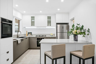 Small contemporary l-shaped eat-in kitchen in Melbourne with a double-bowl sink, flat-panel cabinets, grey cabinets, quartz benchtops, white splashback, subway tile splashback, black appliances, porcelain floors, with island, multi-coloured floor and grey benchtop.