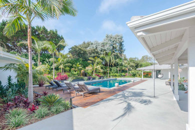 Ejemplo de piscina tropical rectangular en patio trasero con paisajismo de piscina y entablado