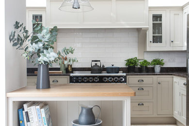 This is an example of a nautical grey and cream kitchen in London with shaker cabinets, white cabinets, white splashback, metro tiled splashback, travertine flooring and a breakfast bar.