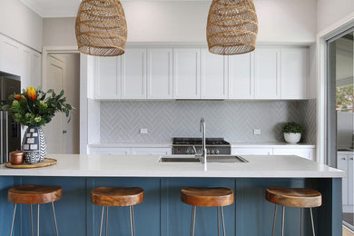 Photo of a mid-sized beach style kitchen in Wollongong with white cabinets, quartz benchtops, subway tile splashback, with island and white benchtop.