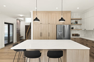 This is an example of a modern kitchen in Calgary with shaker cabinets, light wood cabinets, ceramic splashback, stainless steel appliances and light hardwood flooring.