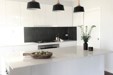 This is an example of a large modern galley open plan kitchen in Wollongong with a submerged sink, flat-panel cabinets, white cabinets, composite countertops, black splashback, ceramic splashback, stainless steel appliances, bamboo flooring, an island and multi-coloured floors.