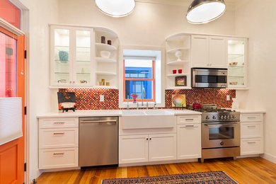 Example of a large trendy single-wall light wood floor enclosed kitchen design in Phoenix with a farmhouse sink, shaker cabinets, white cabinets, solid surface countertops, multicolored backsplash, glass tile backsplash, stainless steel appliances and no island