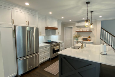 Example of a mid-sized cottage l-shaped dark wood floor and brown floor open concept kitchen design in New York with a farmhouse sink, shaker cabinets, white cabinets, quartz countertops, white backsplash, subway tile backsplash, stainless steel appliances, an island and white countertops