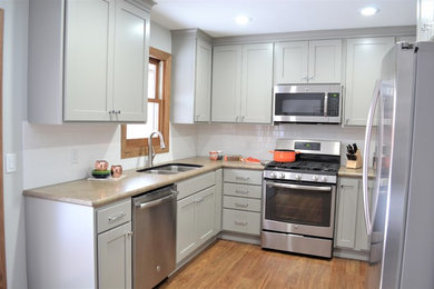 Example of a mid-sized transitional u-shaped vinyl floor and brown floor enclosed kitchen design in Other with an undermount sink, flat-panel cabinets, gray cabinets, laminate countertops, white backsplash, subway tile backsplash, stainless steel appliances and no island