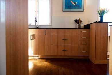 Example of a mid-sized minimalist galley medium tone wood floor open concept kitchen design in Minneapolis with an undermount sink, flat-panel cabinets, light wood cabinets, solid surface countertops, white backsplash, glass tile backsplash, stainless steel appliances and a peninsula