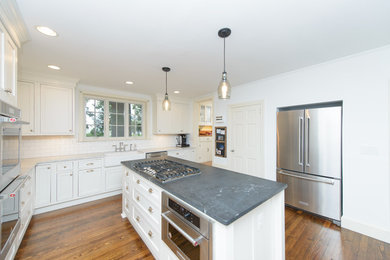 This is an example of a country kitchen in Baltimore with a farmhouse sink, white cabinets, soapstone benchtops, white splashback, subway tile splashback, stainless steel appliances, with island and shaker cabinets.