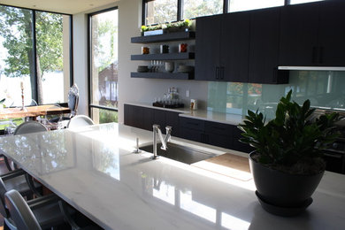 Inspiration for a mid-sized modern l-shaped medium tone wood floor eat-in kitchen remodel in Minneapolis with an undermount sink, flat-panel cabinets, black cabinets, marble countertops, green backsplash, glass sheet backsplash, stainless steel appliances and an island