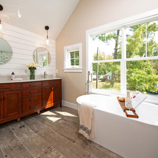 Photo of a transitional master bathroom with shaker cabinets, medium wood cabinets, a freestanding tub, an alcove shower, white tile, beige walls, wood-look tile, an undermount sink, engineered quartz benchtops, brown floor, a sliding shower screen, beige benchtops, a double vanity, a built-in vanity, vaulted and planked wall panelling.
