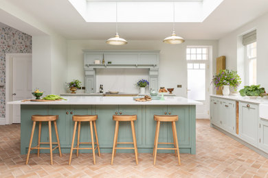 Photo of a large classic kitchen/diner in Other with a belfast sink, shaker cabinets, green cabinets, marble worktops, white splashback, black appliances, brick flooring, an island, red floors, white worktops and a feature wall.