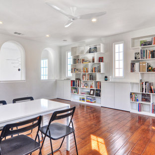 This is an example of an expansive modern home studio in Orange County with white walls, medium hardwood flooring, no fireplace and a freestanding desk.
