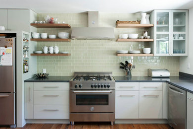 Transitional medium tone wood floor kitchen photo in Other with flat-panel cabinets, white cabinets, solid surface countertops, green backsplash, glass tile backsplash and stainless steel appliances