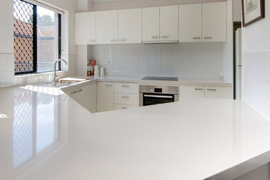 Small modern u-shaped eat-in kitchen in Brisbane with a single-bowl sink, flat-panel cabinets, yellow cabinets, quartz benchtops, white splashback, ceramic splashback, stainless steel appliances, ceramic floors and no island.