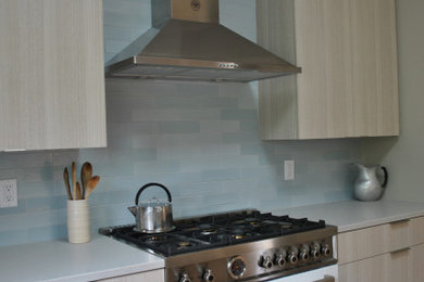 Example of a large minimalist l-shaped medium tone wood floor enclosed kitchen design in Providence with an undermount sink, flat-panel cabinets, laminate countertops, blue backsplash, ceramic backsplash, stainless steel appliances, an island and gray countertops
