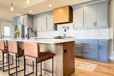 Inspiration for a mid-sized farmhouse light wood floor eat-in kitchen remodel in Other with a farmhouse sink, shaker cabinets, blue cabinets, quartz countertops, white backsplash, ceramic backsplash, stainless steel appliances, an island and white countertops