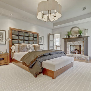 Foto på ett stort vintage huvudsovrum, med vita väggar, mellanmörkt trägolv, brunt golv, en standard öppen spis och en spiselkrans i sten