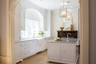 Example of a large classic medium tone wood floor and brown floor kitchen design in Chicago with a farmhouse sink, recessed-panel cabinets, white cabinets, white backsplash, subway tile backsplash, paneled appliances and an island